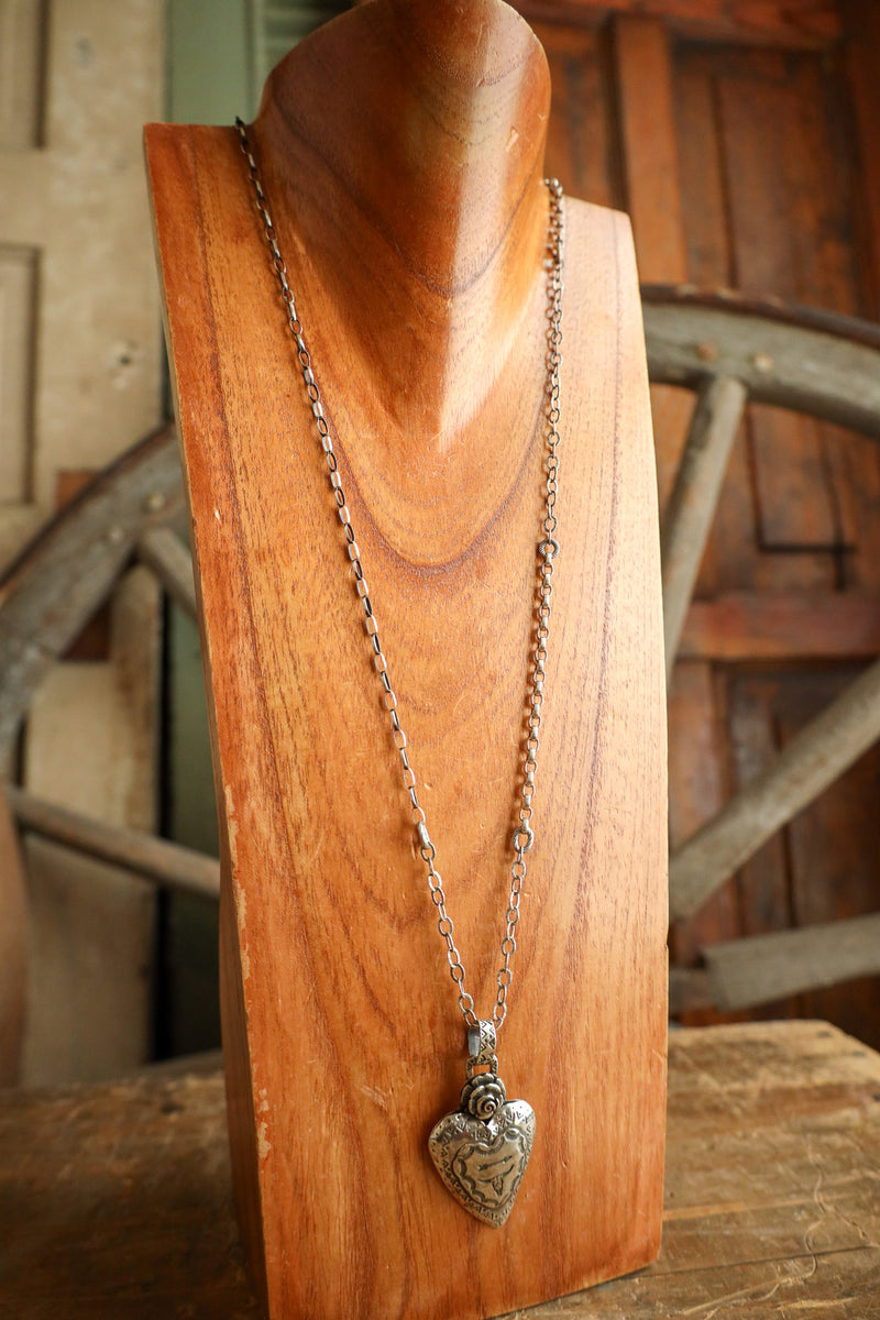 Silver heart-shaped pendant necklace on a wooden stand with a rustic background
