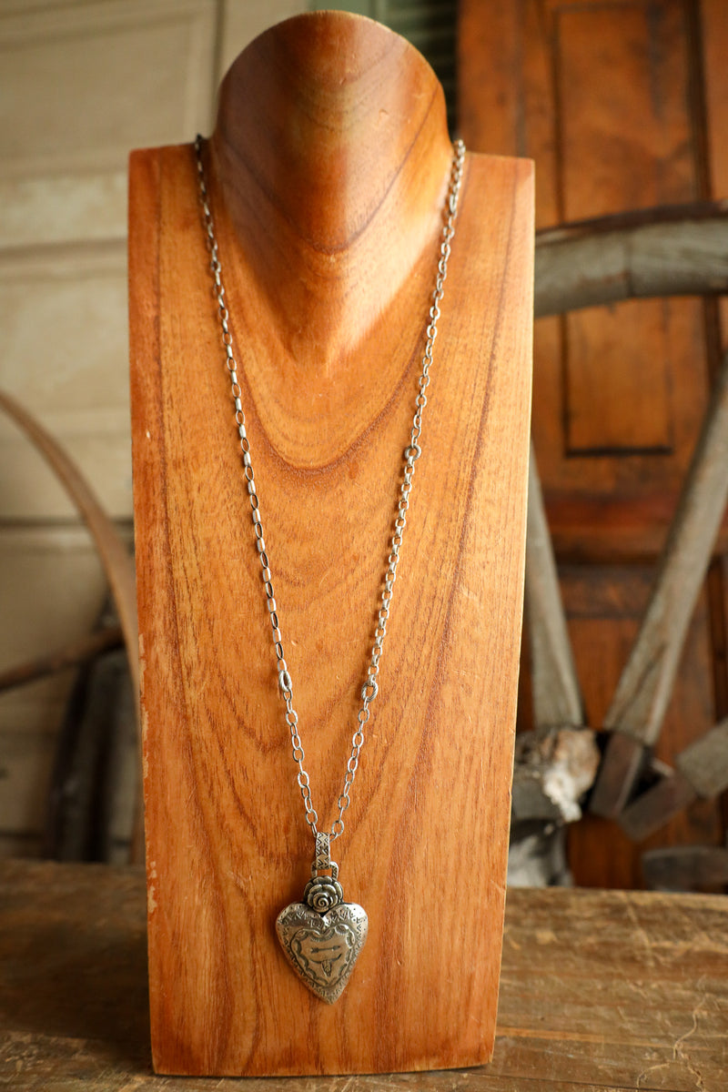 Silver necklace with a heart pendant on a wooden stand.