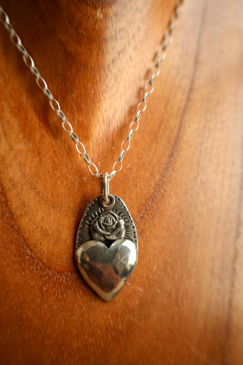 Silver heart-shaped pendant with rose design on a chain against a wooden background