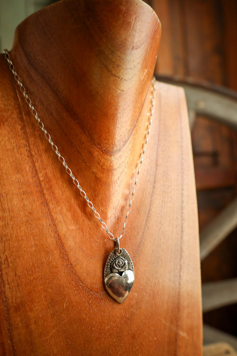 Silver necklace with a heart-shaped pendant on a wooden mannequin.