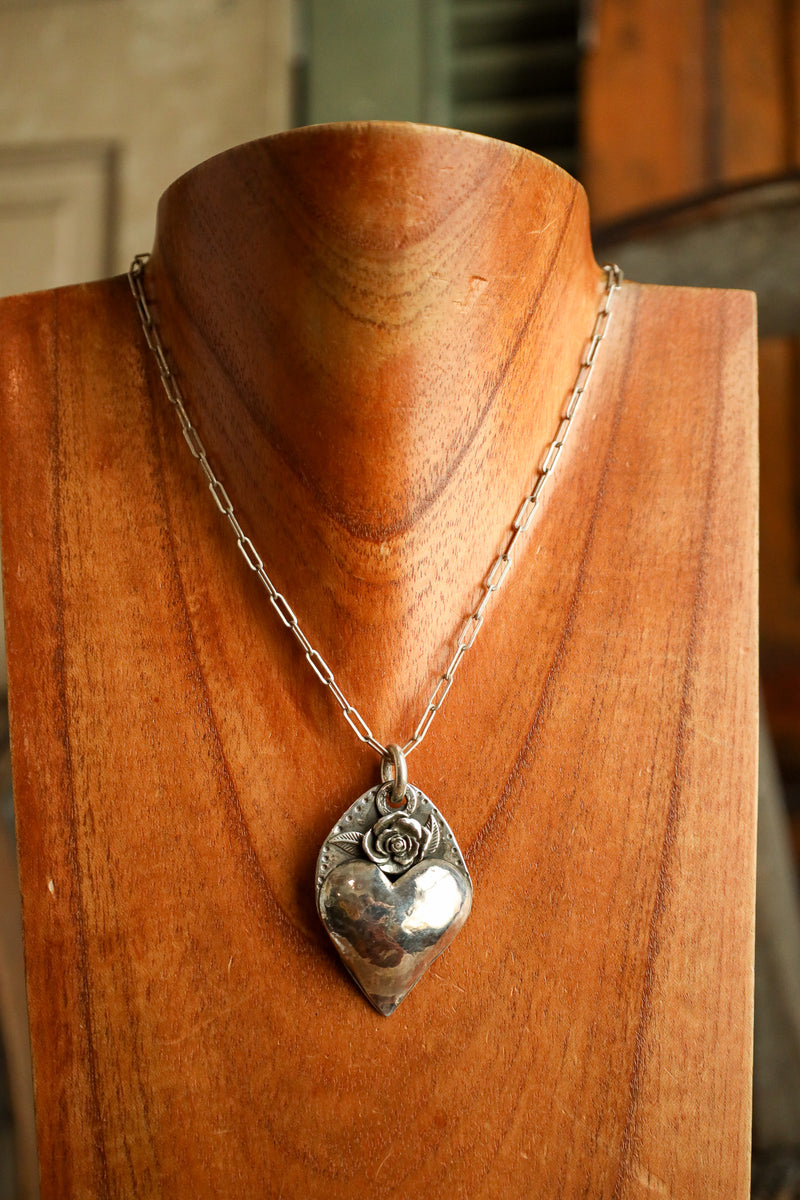 Silver necklace with a heart-shaped pendant on a wooden mannequin
