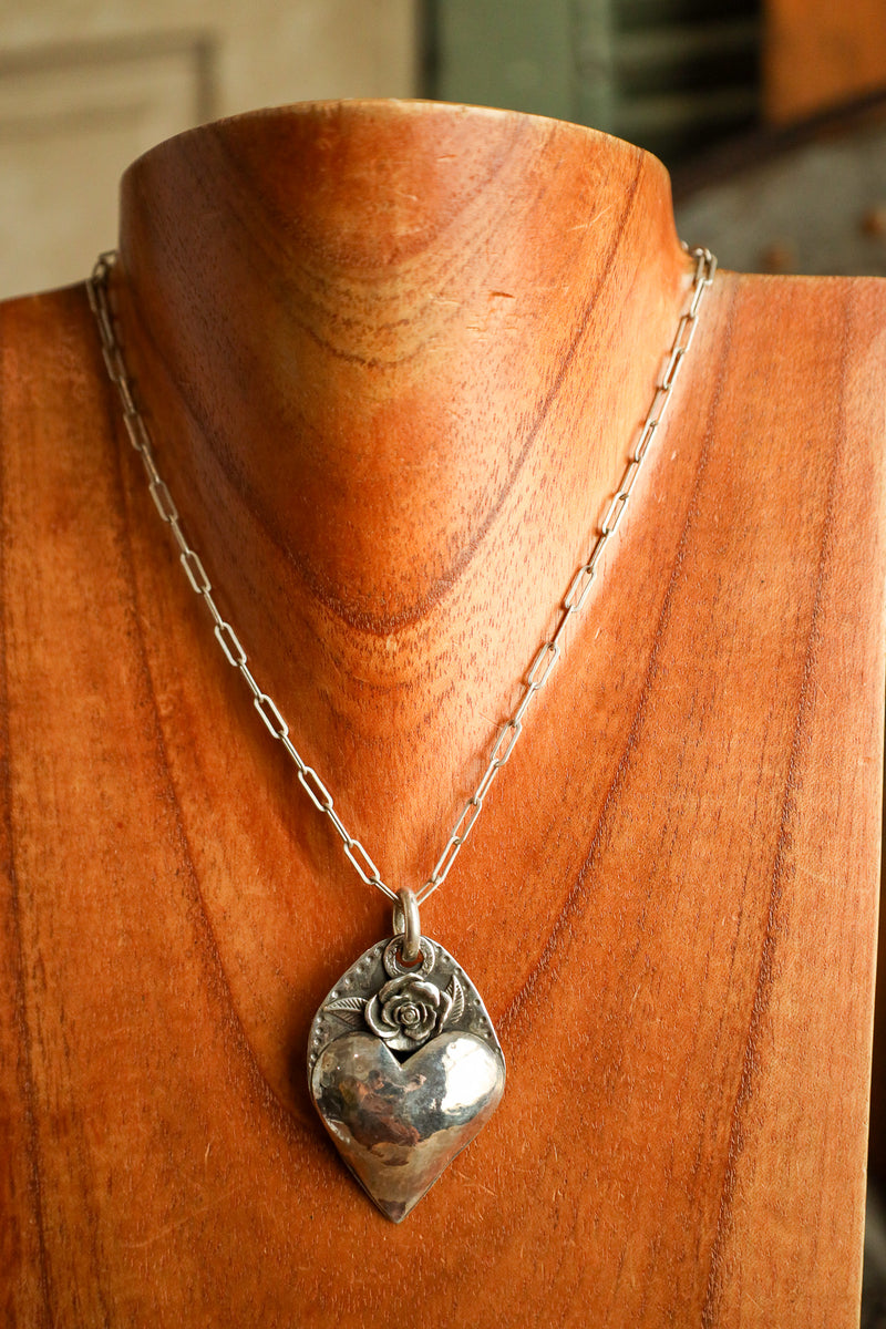Silver necklace with a heart-shaped pendant on a wooden mannequin