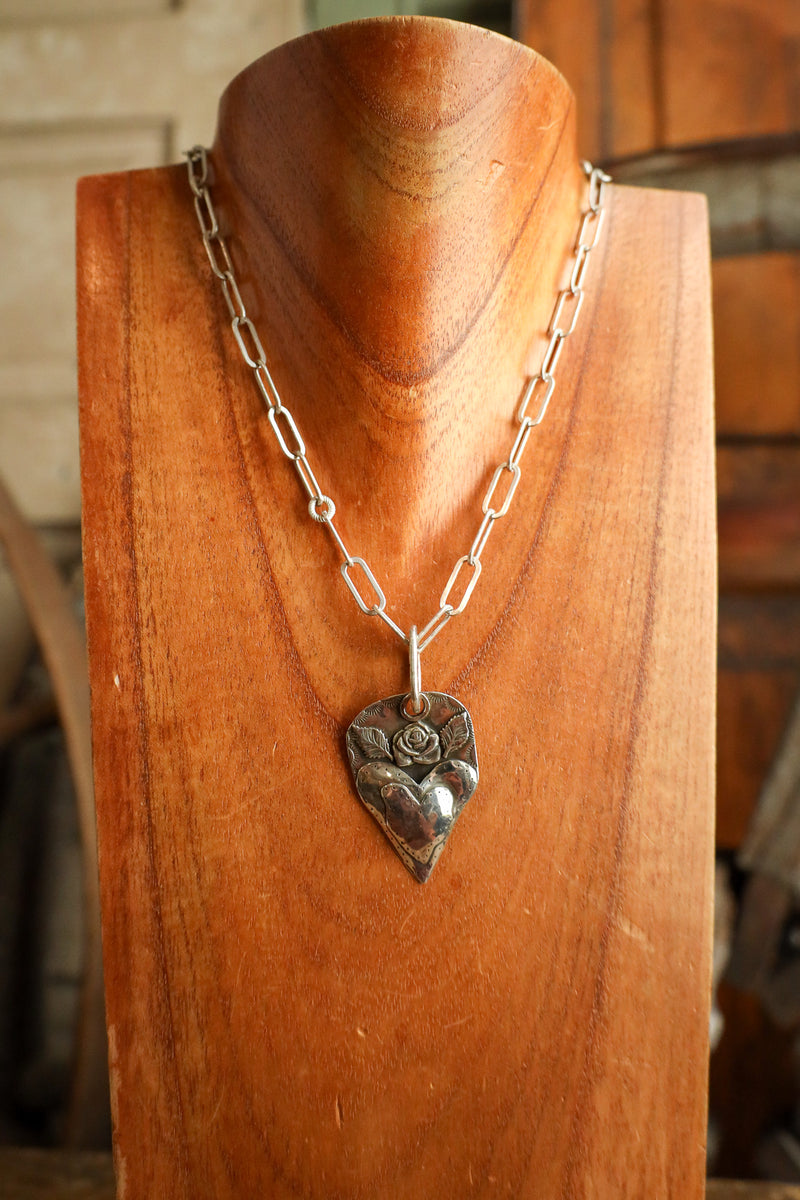 Silver heart-shaped pendant necklace on a wooden stand