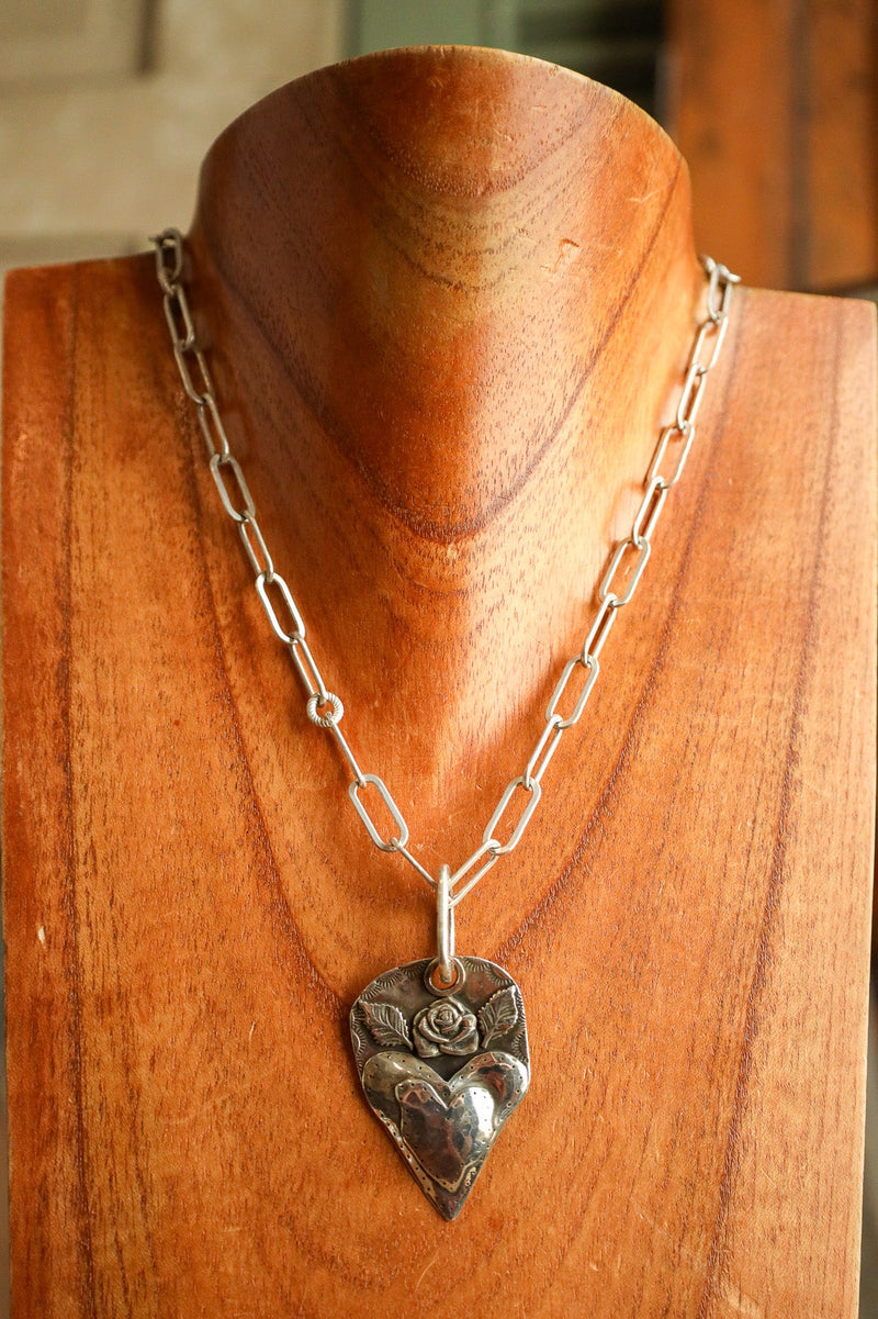 Silver necklace with a heart-shaped pendant on a wooden mannequin