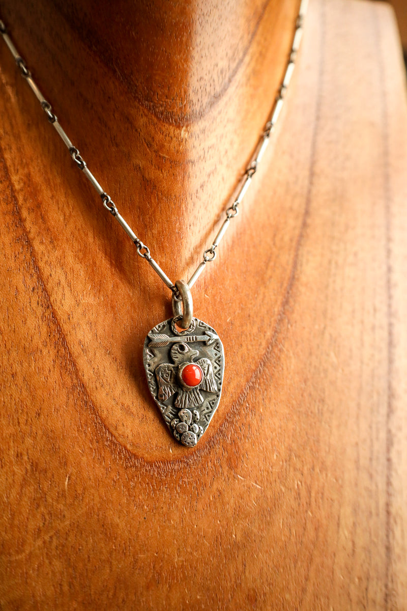Silver pendant necklace with a red stone on a wooden surface