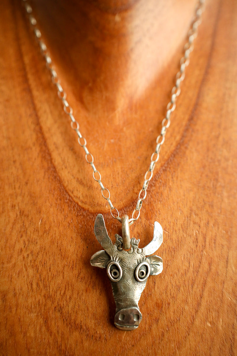Silver cow head pendant on a chain against a wooden background