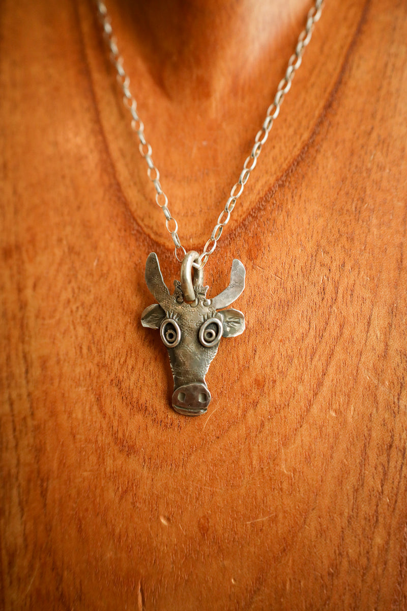 Silver cow head pendant necklace on a wooden background