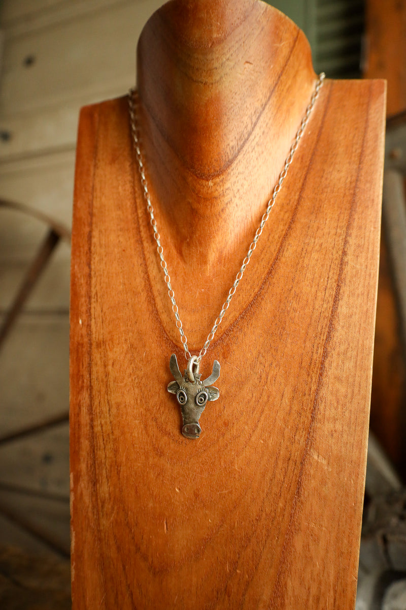 Silver necklace with a deer head pendant on a wooden stand.