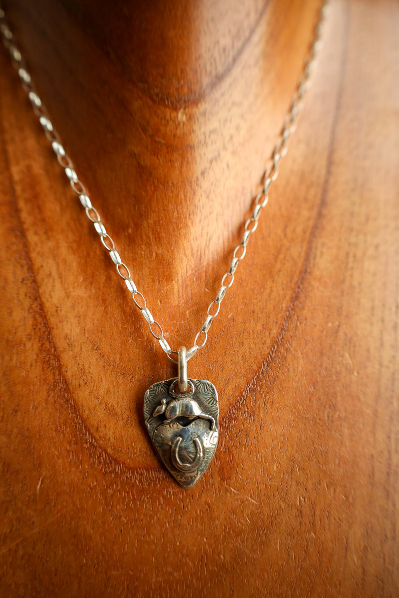 Silver necklace with a shield-shaped pendant on a wooden surface