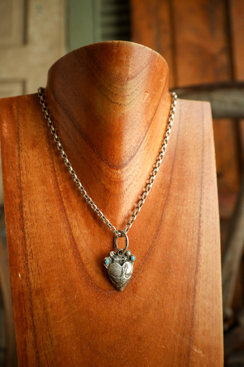 Silver necklace with a heart-shaped pendant on a wooden mannequin bust.