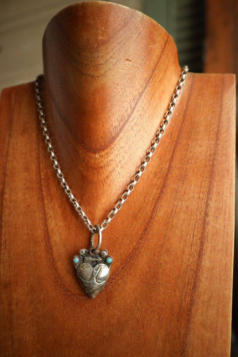 Silver necklace with a heart-shaped pendant on a wooden mannequin