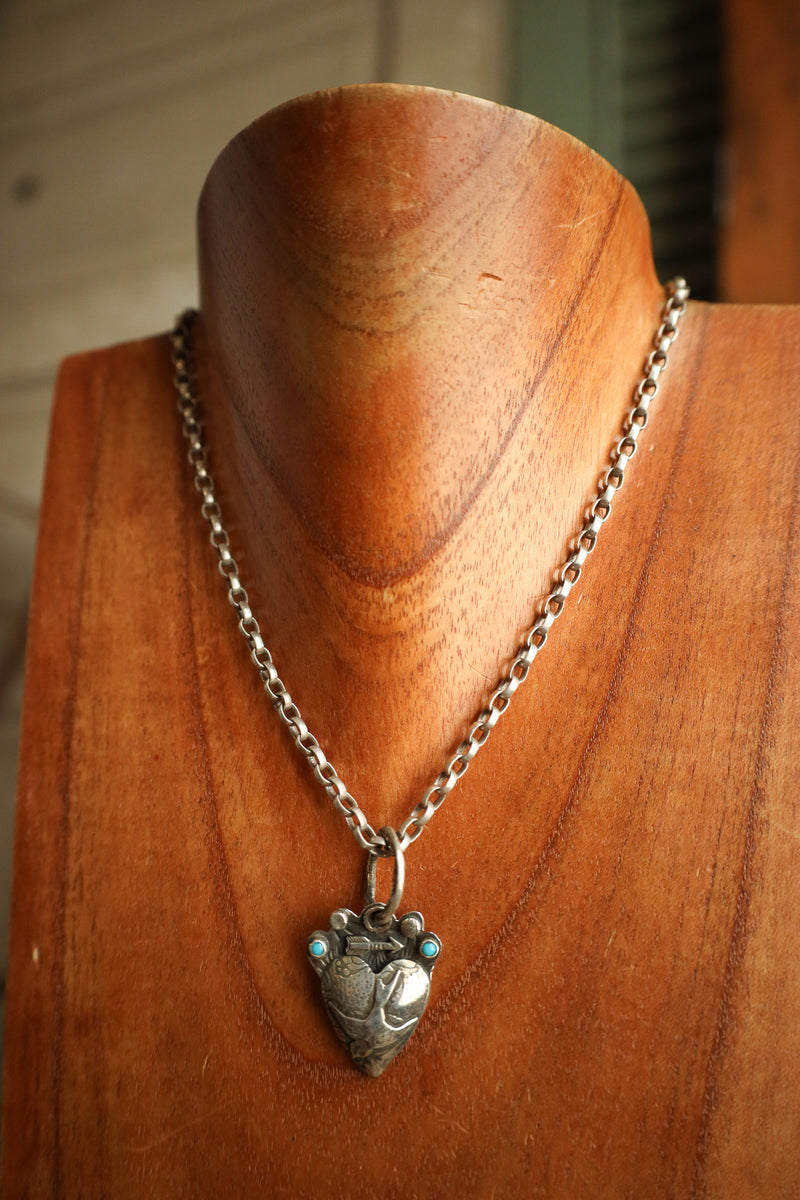Silver necklace with a heart-shaped pendant on a wooden mannequin