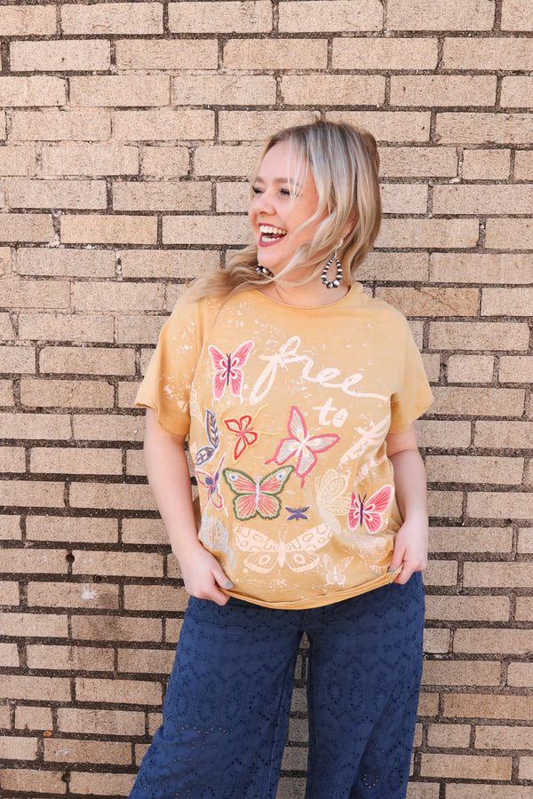Woman wearing yellow short sleeve tee with script "Free to fly" with butterflies embroidered  on.