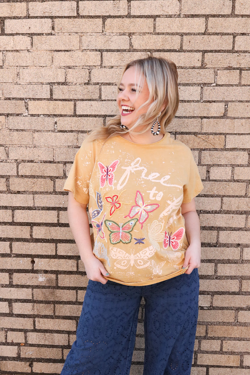 Woman wearing yellow short sleeve tee with script "Free to fly" with butterflies embroidered  on.