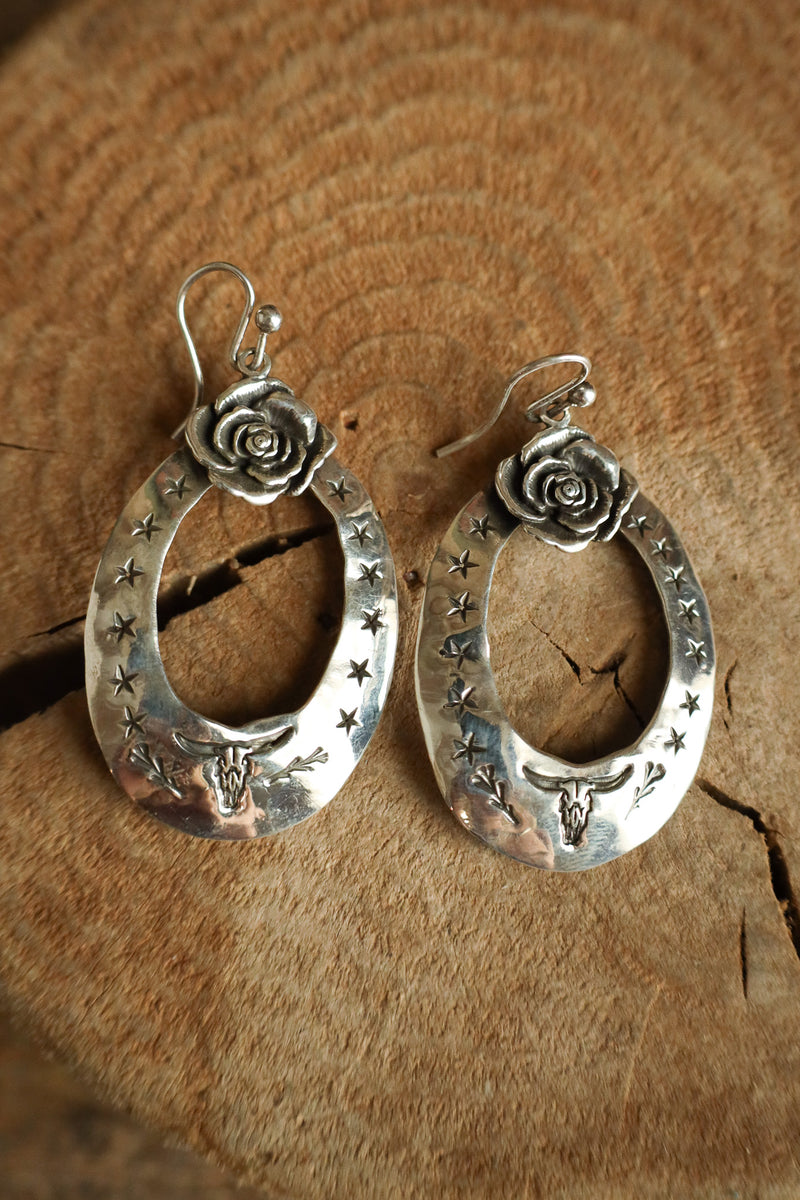 Silver hoop earrings with rose and star designs on a wooden surface
