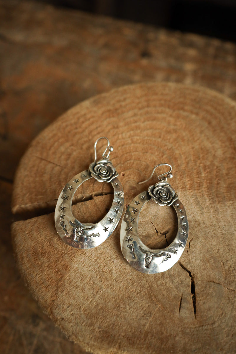 Silver hoop earrings with floral designs on a wooden surface