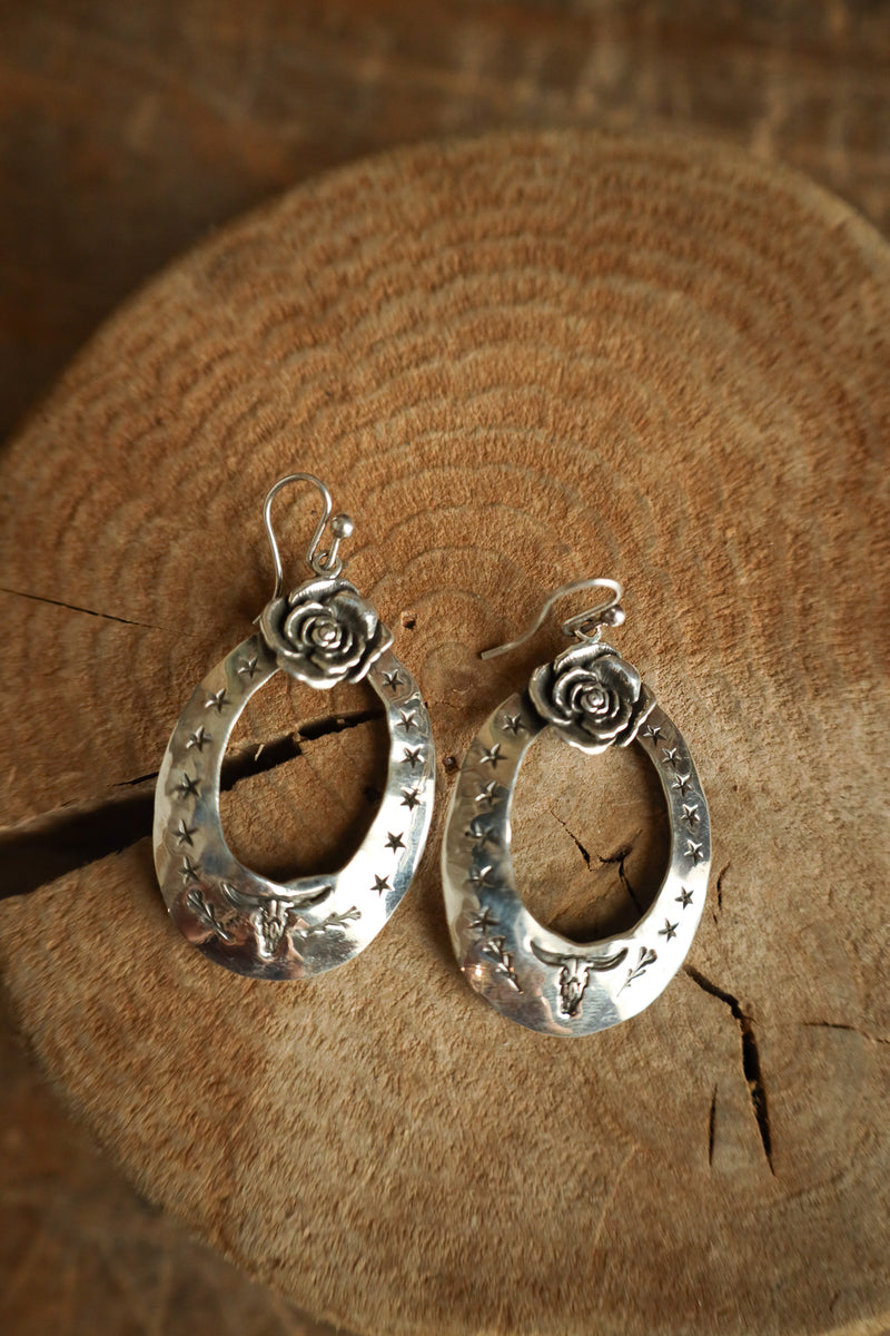 Silver hoop earrings with floral designs on a wooden surface