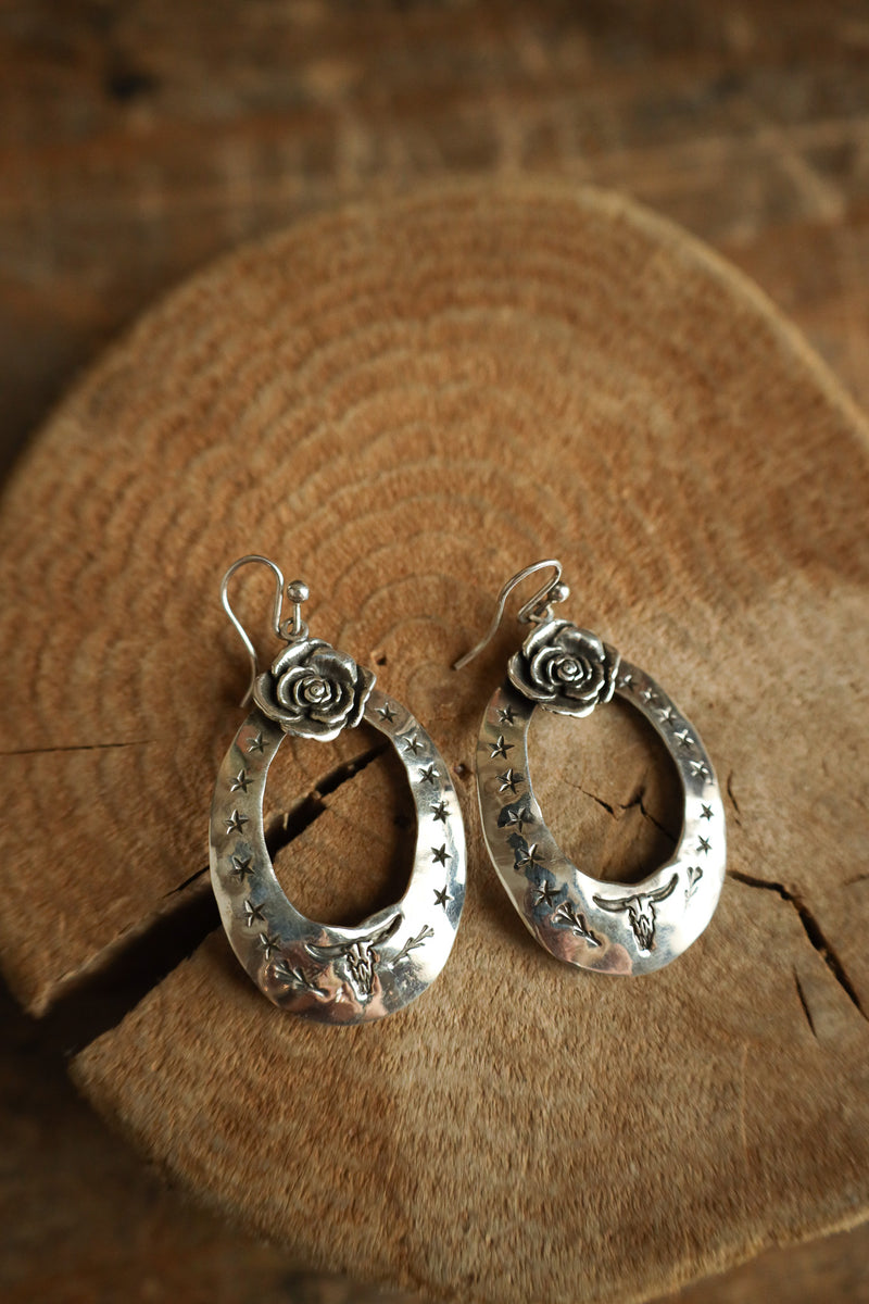 Pair of silver earrings with floral designs on a wooden surface