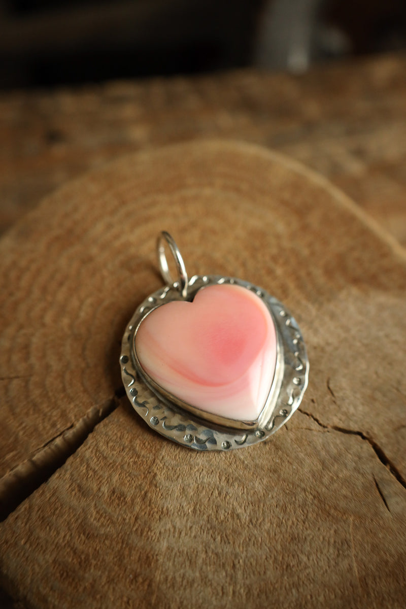Pink heart-shaped pendant on a textured wooden surface