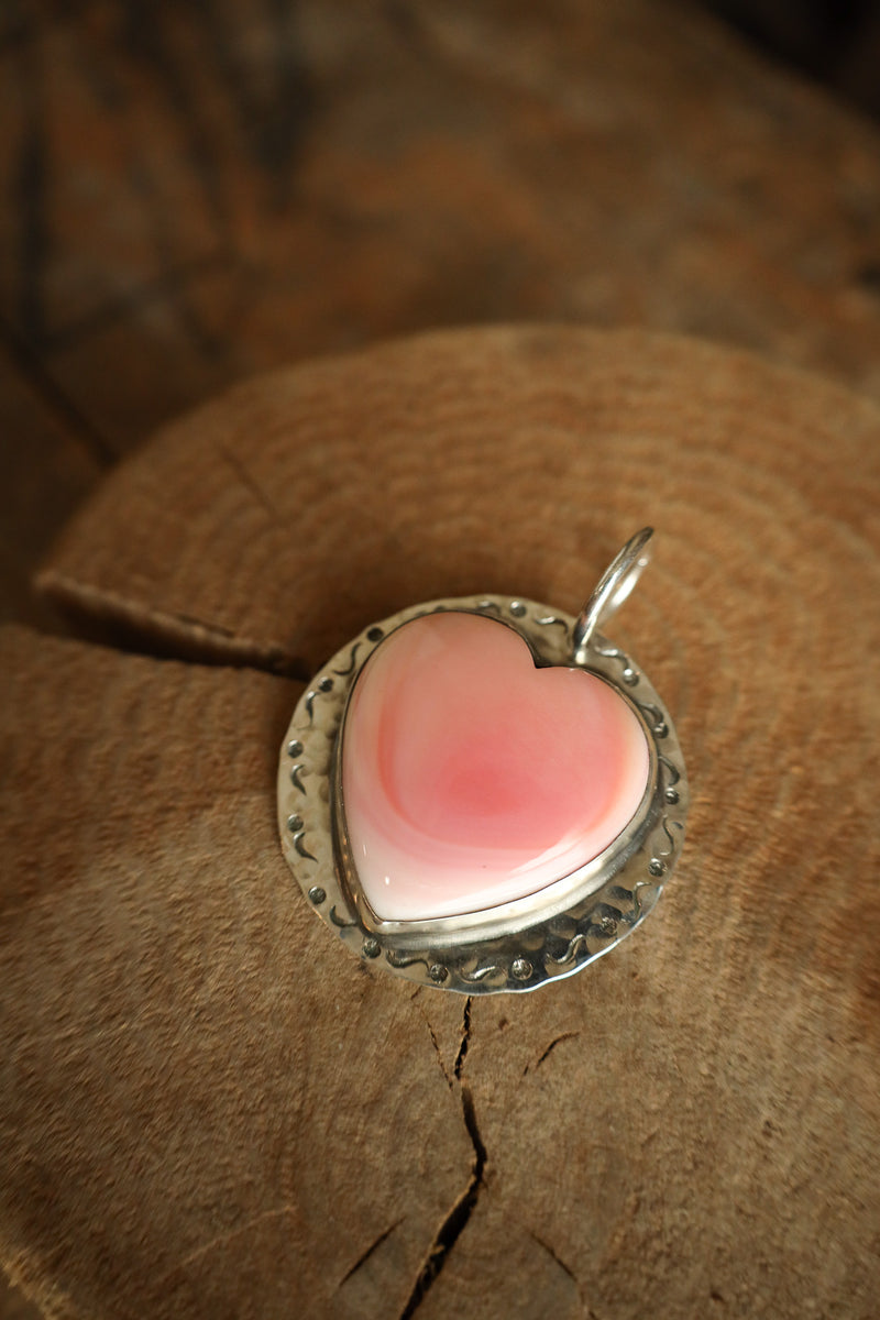 Heart-shaped pink pendant with silver border on a wooden surface