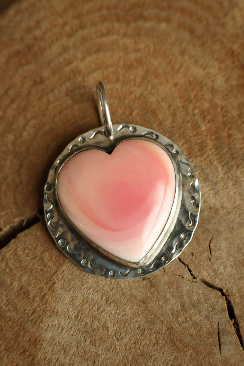 Pink heart-shaped pendant with silver border on a wooden surface