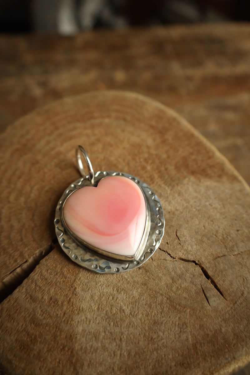 Heart-shaped pink pendant with silver border on a wooden surface