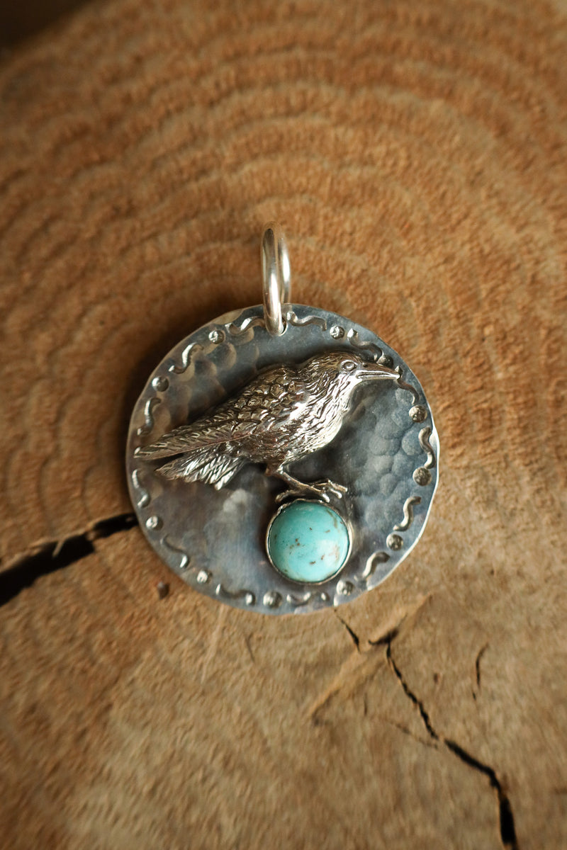 Silver pendant with a bird design and turquoise stone on a wooden surface