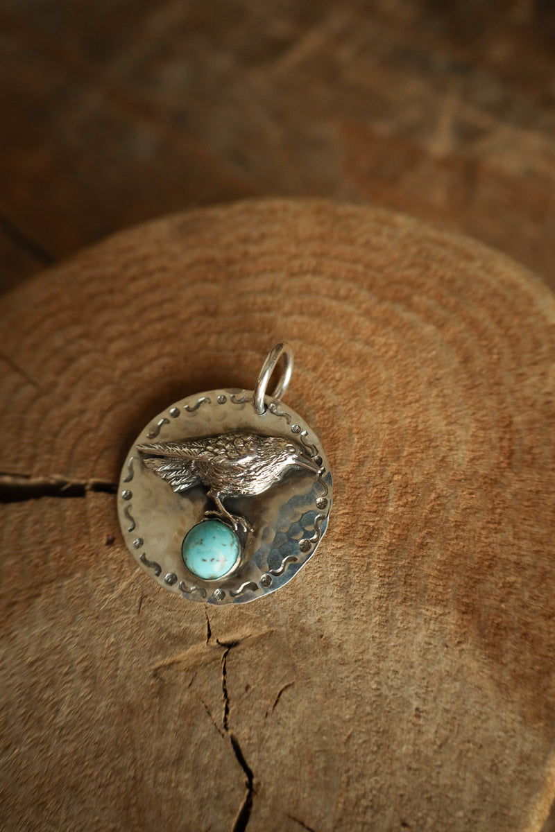 Silver pendant with a bird design and turquoise stone on a wooden surface