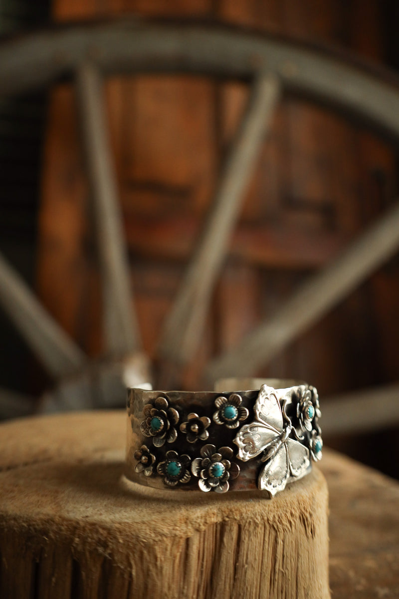 Silver cuff bracelet with floral designs on a wooden surface with a rustic background