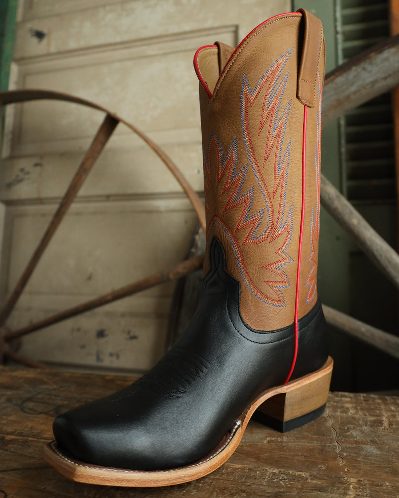 Cowboy boot with tan top and black sole on a wooden surface