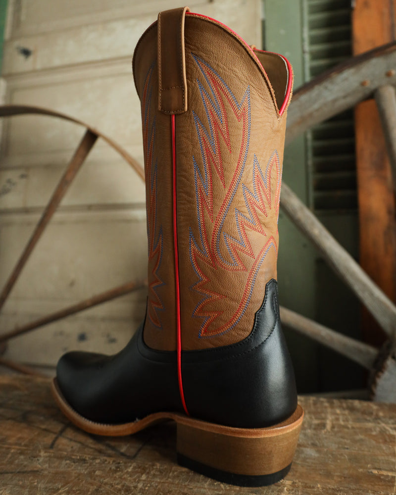 Brown and black cowboy boot with red stitching on a wooden surface.