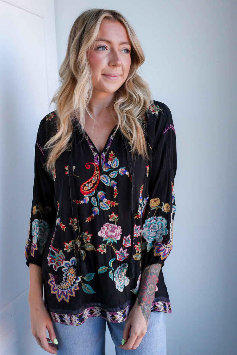 Woman wearing a black floral blouse against a white wall