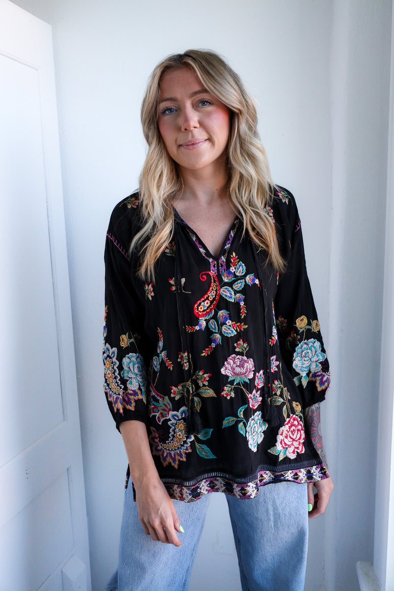 Woman wearing a black floral embroidered blouse against a white background