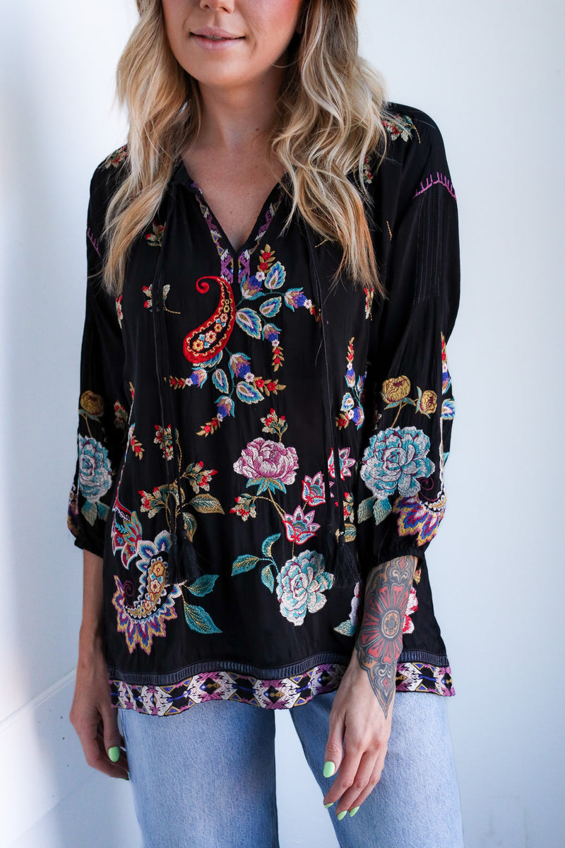 Woman wearing a black floral embroidered blouse against a white background