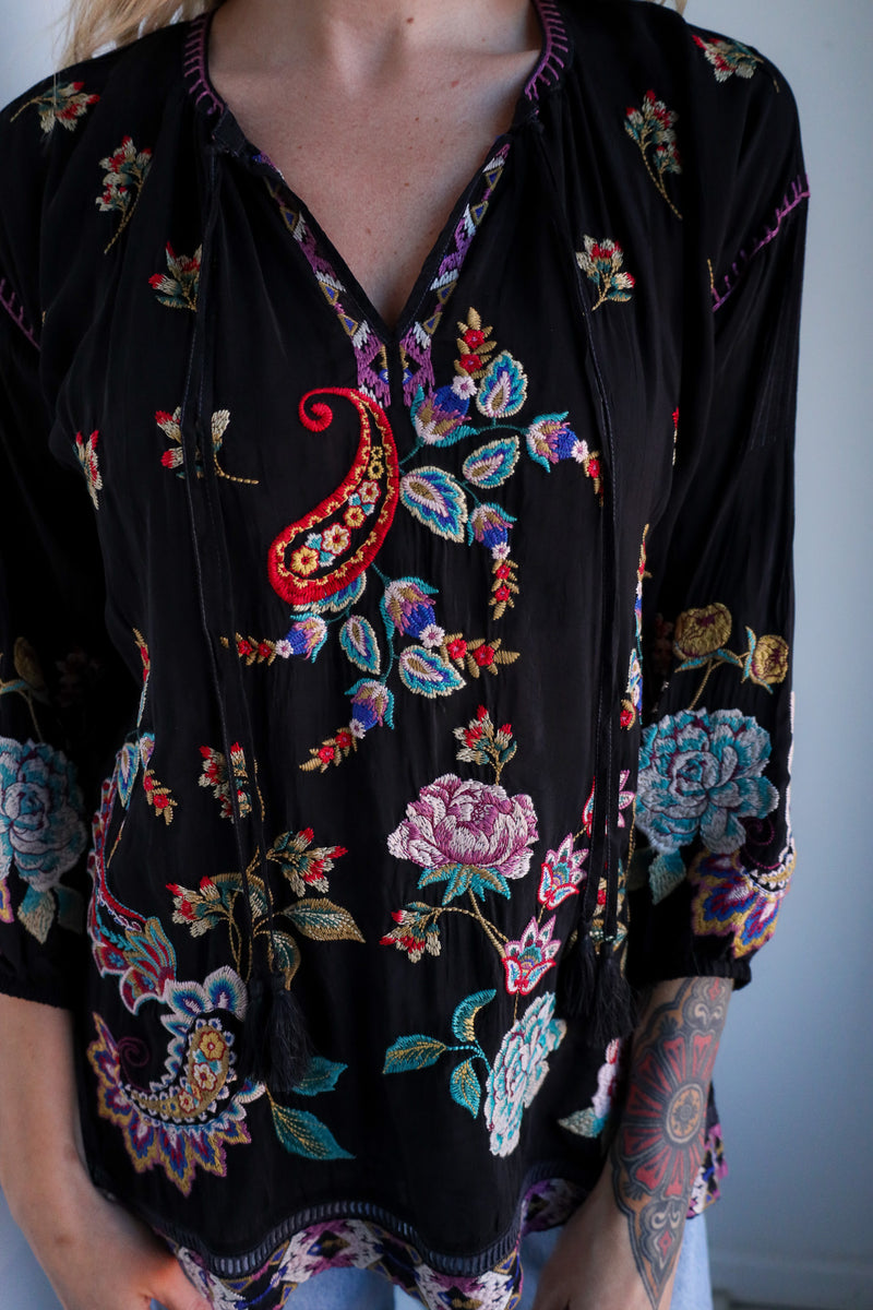 Black floral embroidered top worn by a person against a plain background