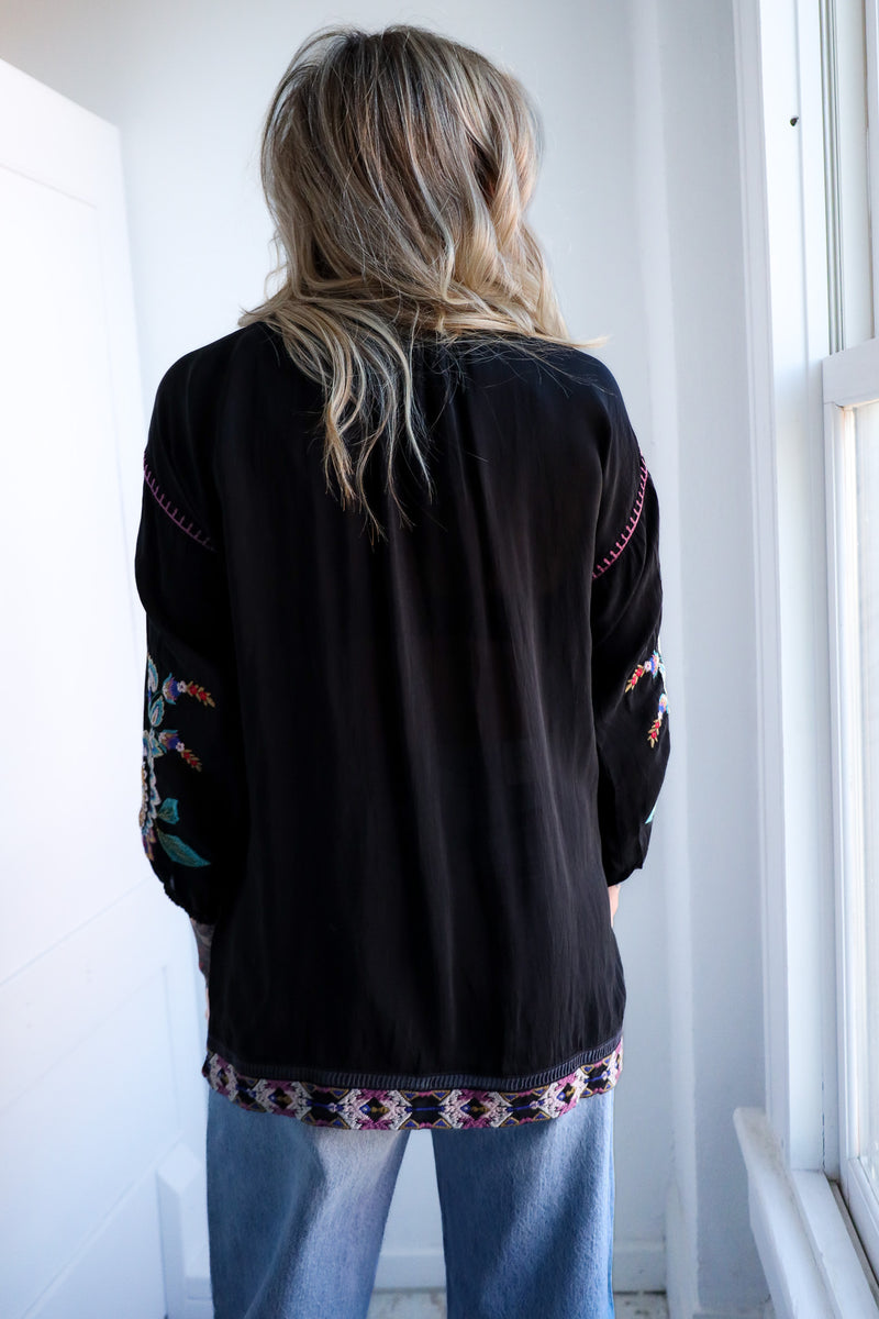 Person wearing a black embroidered jacket in a bright room