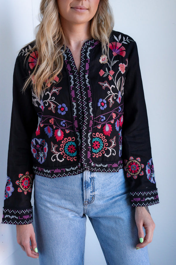 Woman wearing a black embroidered jacket with colorful patterns against a white background