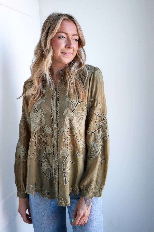 Woman wearing a green embroidered blouse against a white background