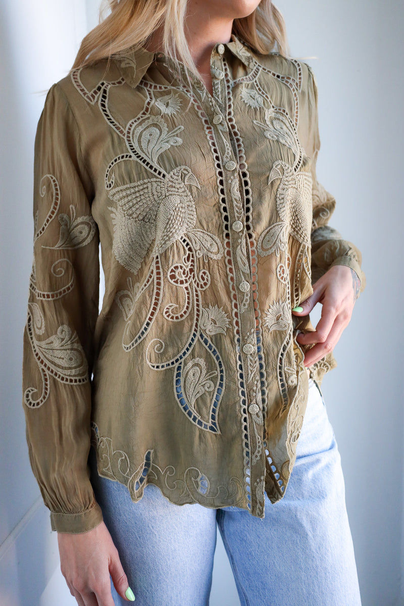 Woman wearing a beige embroidered blouse with long sleeves against a plain background