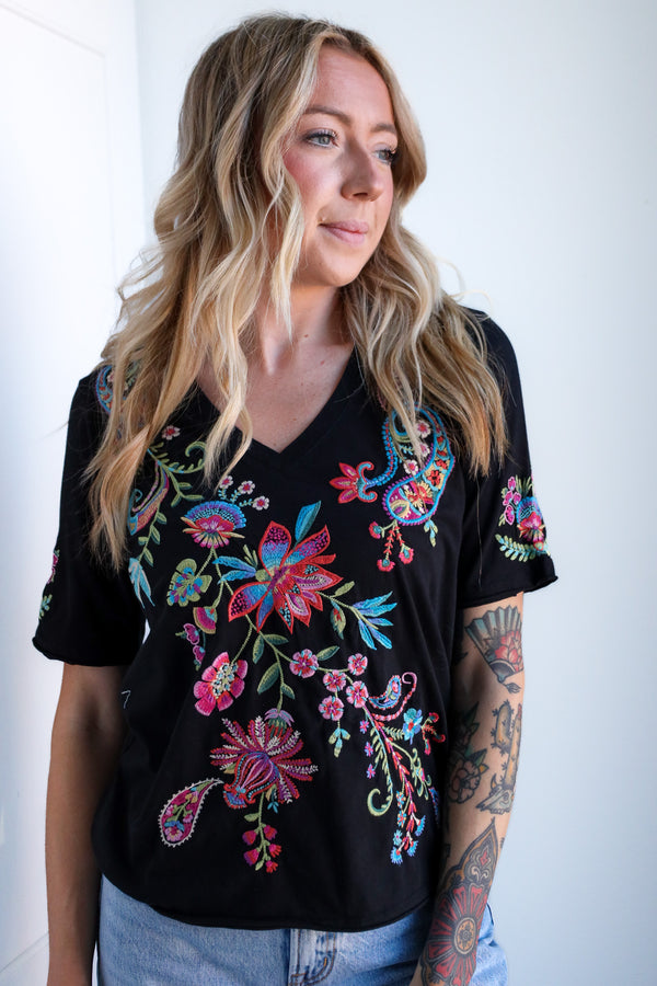 Woman wearing a black top with colorful floral embroidery against a white background