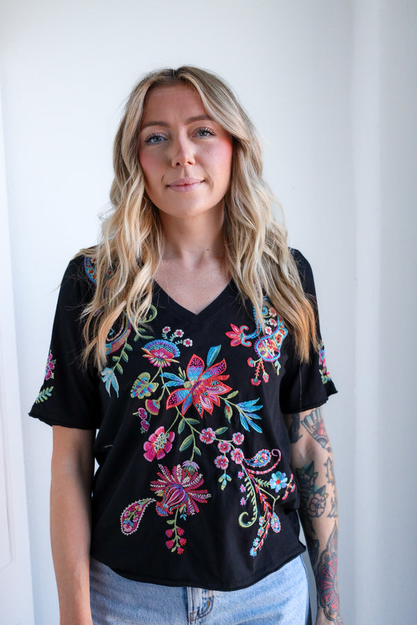 Woman wearing a black top with colorful floral embroidery against a white background