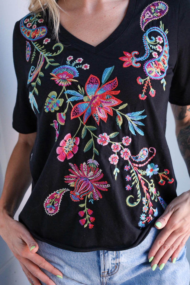 Black t-shirt with colorful floral embroidery worn by a person.