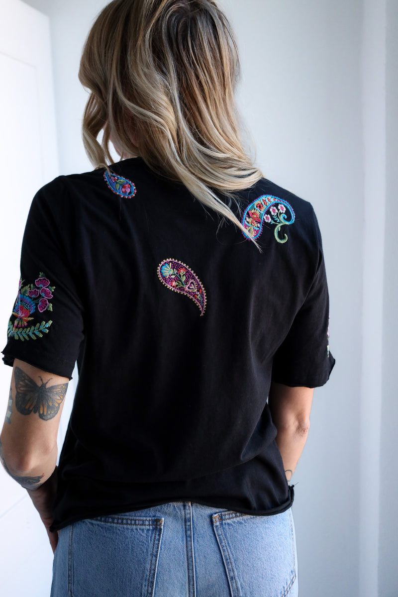 Person wearing a black t-shirt with colorful embroidery on a white background