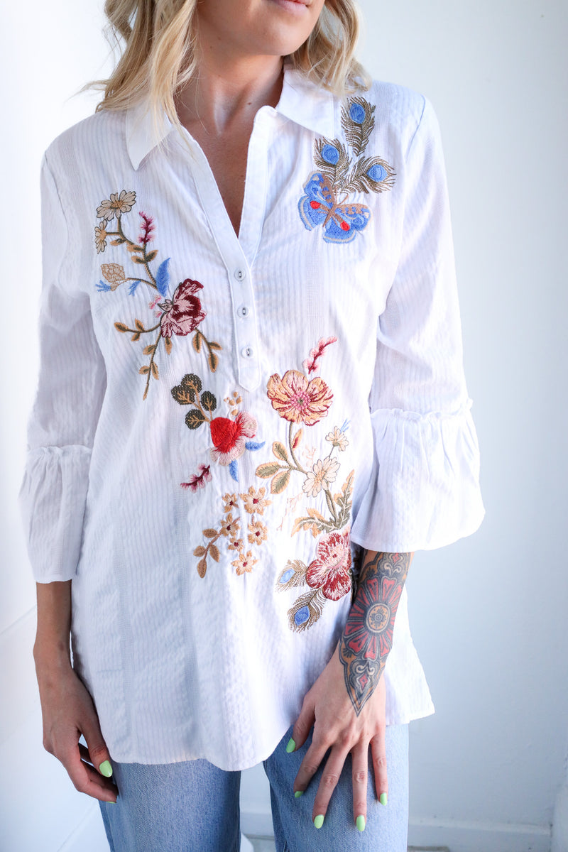 White shirt with colorful floral embroidery worn by a person against a light background