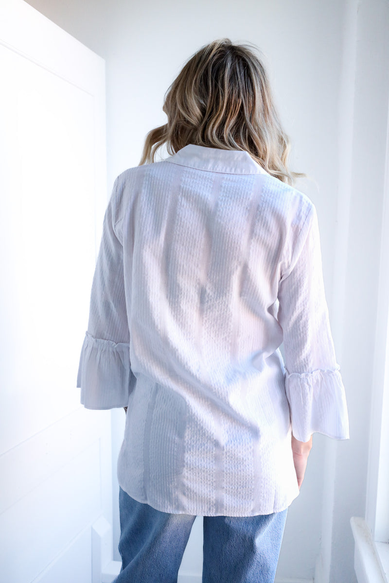 Person wearing a white blouse with ruffled sleeves against a white background