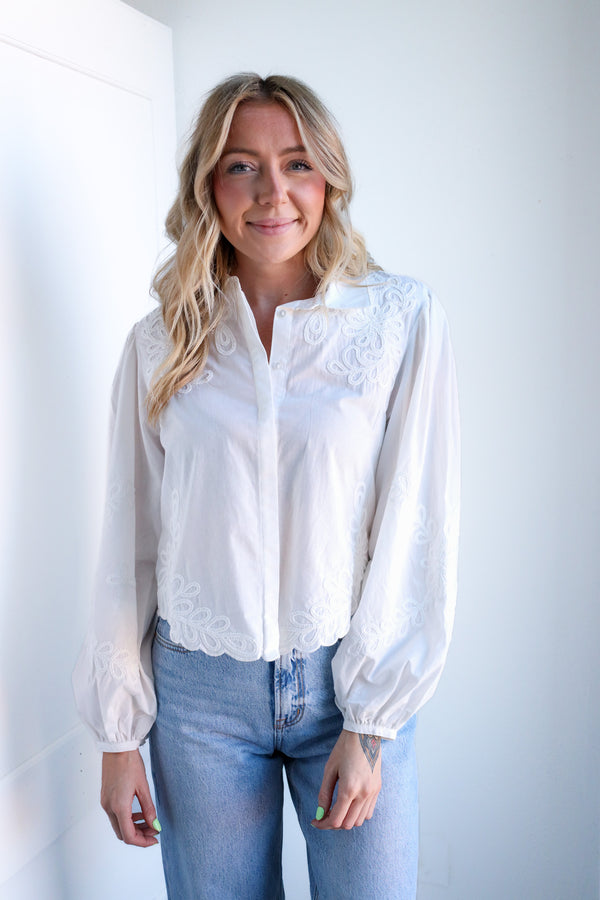 Woman wearing a white blouse with lace details and blue jeans against a plain background