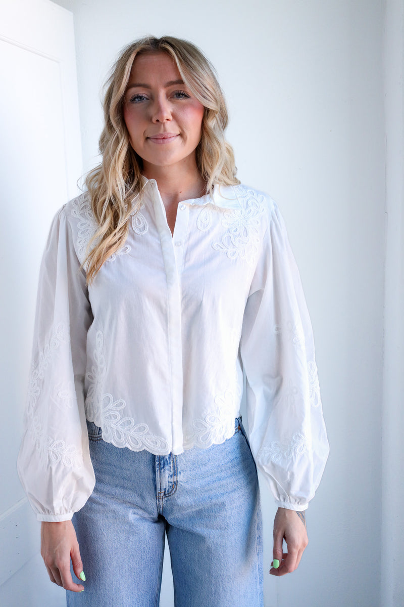 Woman wearing a white blouse with lace details and blue jeans against a plain background