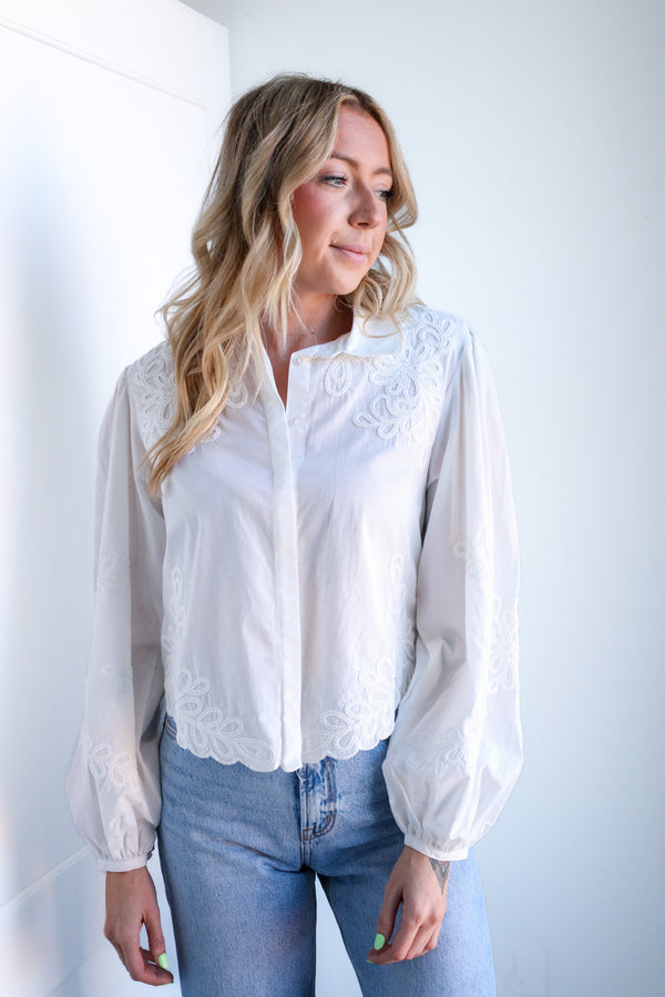 Woman wearing a white blouse with lace details and blue jeans against a plain background