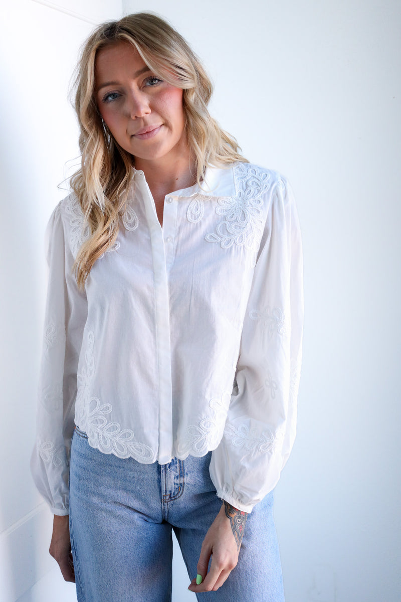 Woman wearing a white blouse with lace details and blue jeans on a plain background