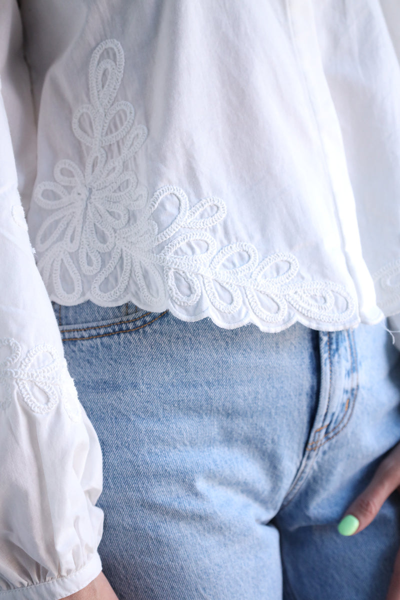 White lace-trimmed blouse over denim jeans with a blurred background